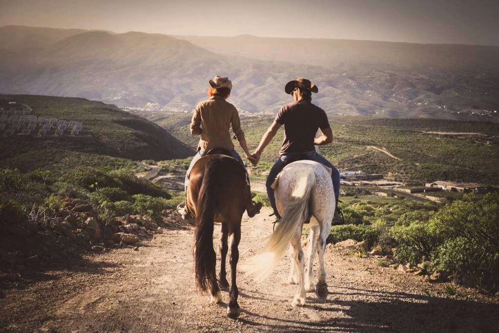 Cowboy and cowgirl riding horses together while holding hands
