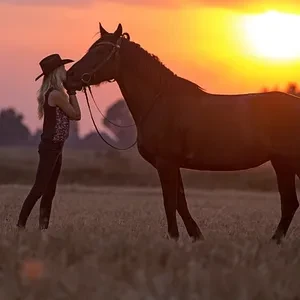 Blonde Woman in Cowboy Hat Touching Horse at Sunset - FarmersOnly